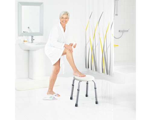Helles Badezimmer mit einer Frau im Bademantel, die auf einem Duschhocker sitzt
