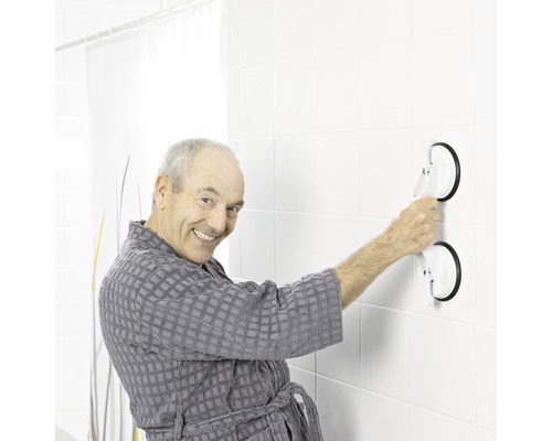 Ein Mann im Bademantel befestigt einen Haltegriff mit Saugnäpfen an einer gefliesten Wand.