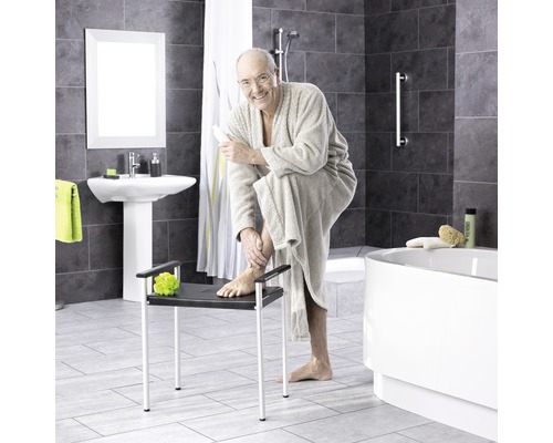 Badezimmer mit Badewanne, Waschbecken und einer Person, die auf einem Duschhocker sitzt
