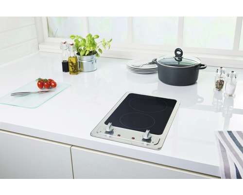 Küchenszene mit Kochfeld, Topf, Schneidebrett und Küchenutensilien auf einer weißen Arbeitsplatte.