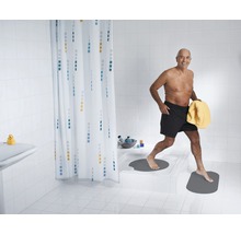 Helles Badezimmer mit Duschvorhang, Badematten und einer Person mit Handtuch