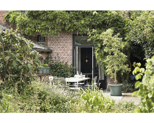 Außenbereich mit Tisch, Stühlen und Pflanzen vor einem Backsteingebäude