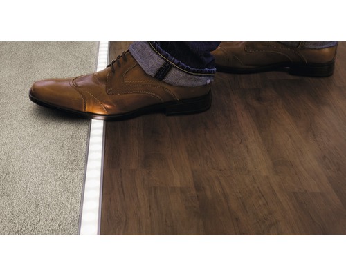 Person betritt Holzboden von Teppich über LED-Profil