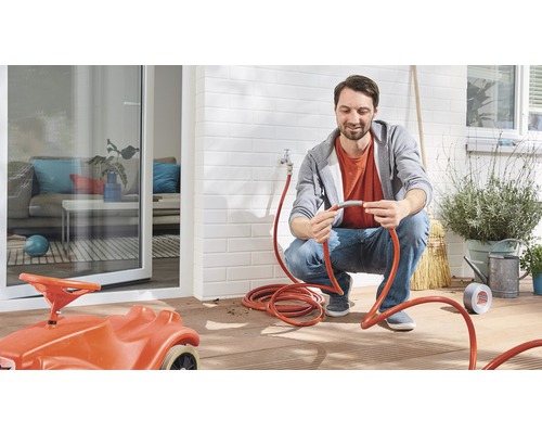 Mann schliesst einen Gartenschlauch an einen Wasserhahn im Aussenbereich an