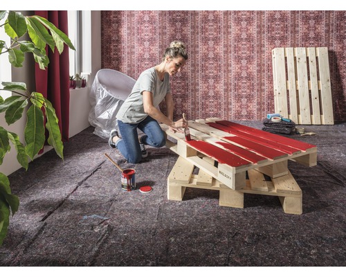 Frau streicht Holzpalette mit Farbe für ein DIY Projekt