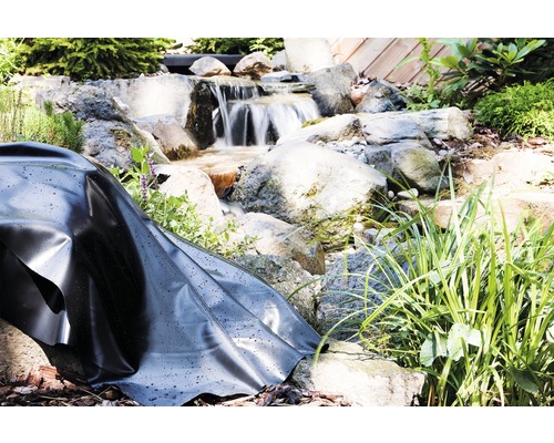 Teichfolie in einem angelegten Gartenteich mit Wasserfall und Steinen.