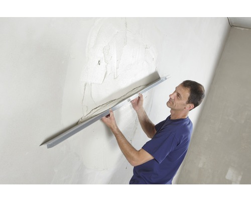 Mann glättet Putz an einer Wand mit einer Glättkelle