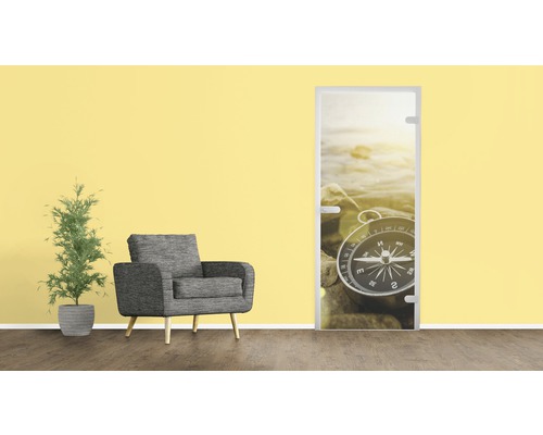 Zimmertür mit Kompass Motiv, Sessel und Topfpflanze vor einer gelben Wand