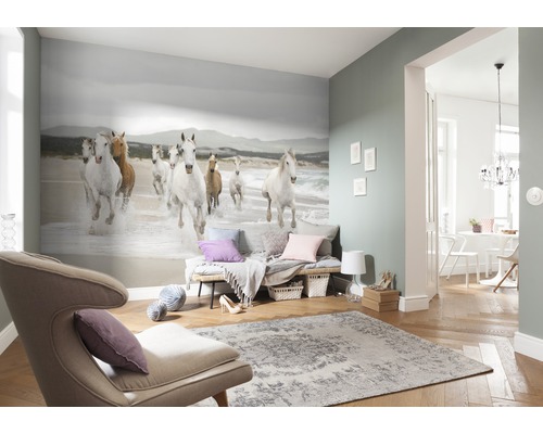 Wohnzimmer mit Fototapete, die eine Gruppe galoppierender Pferde am Strand zeigt, dazu Sessel und Teppich