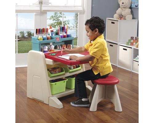Kind sitzt an einem Kinderschreibtisch mit Stuhl und malt auf Papier