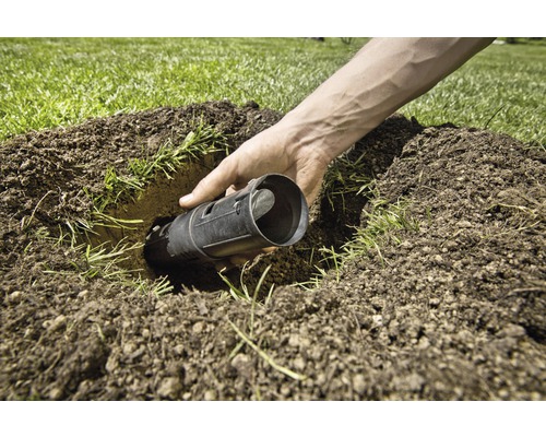 Eine Person setzt eine Maulwurfsfalle in ein Loch im Rasen.