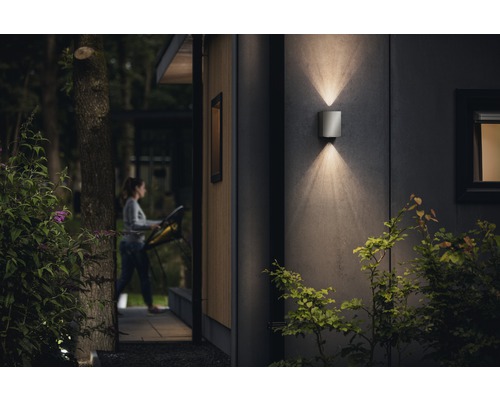 Moderne Hausfassade mit leuchtender Wandleuchte und Frau im Hintergrund