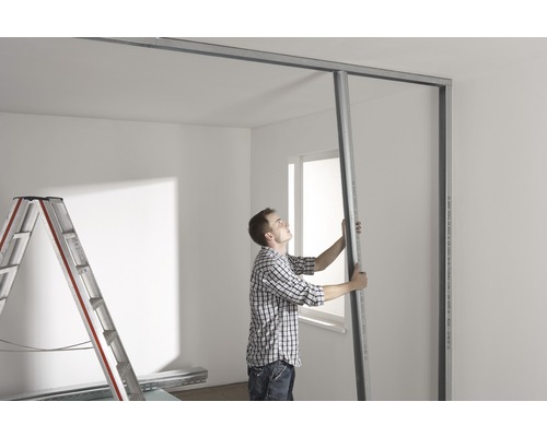 Mann montiert eine Metallkonstruktion für eine Trockenbauwand in einem Raum.