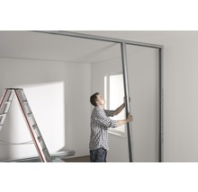 Mann montiert Metallprofile für Trockenbauwand in einem Raum.