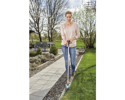 Frau verwendet einen Rasenkantenschneider im Garten, um Rasenkanten zu schneiden.