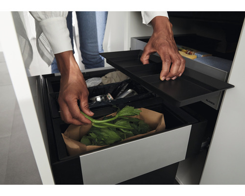 Eine Person wirft Küchenabfälle in einen Mülleimer mit mehreren Fächern. Der Mülleimer ist in einem Küchenschrank integriert.