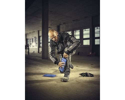 Ein Mann befestigt Knieschoner an seinem Bein auf einer Baustelle
