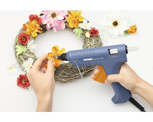 Person klebt mit Heißklebepistole Blumen auf einen Kranz