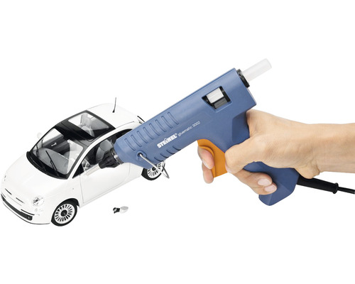 Heißklebepistole in der Hand vor einem Spielzeugauto