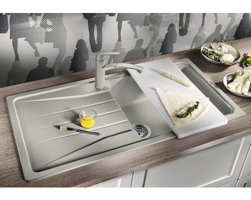 Küchenspüle mit Armatur, Schneidebrett und Speisen auf einer Küchentheke.