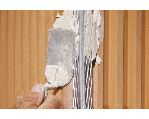 Dünnbettmörtel wird mit einer Kelle auf eine Ziegelwand aufgetragen.