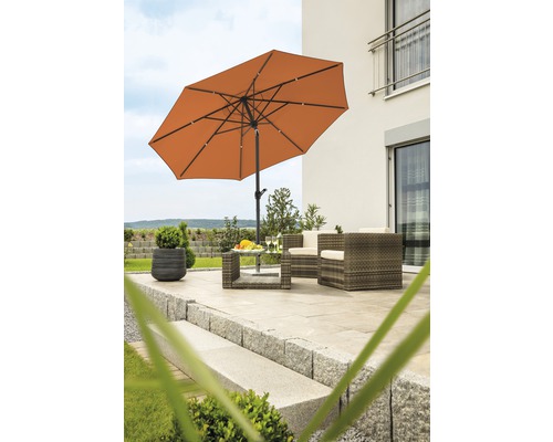 Szene mit Sonnenschirm, Gartenmöbeln und dekorativen Elementen auf einer Terrasse