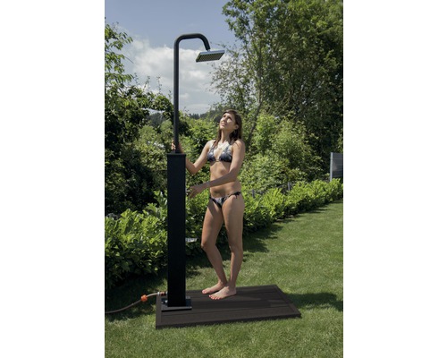 Gartenszene mit einer Frau unter einer Außendusche auf einer Holzterrasse.