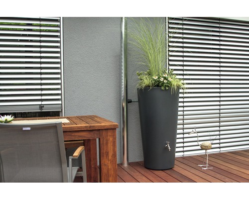 Szene mit Regenspeicher, bepflanzt mit Blumen und Gräsern, neben einer Regenrinne, auf einer Terrasse mit Holzboden