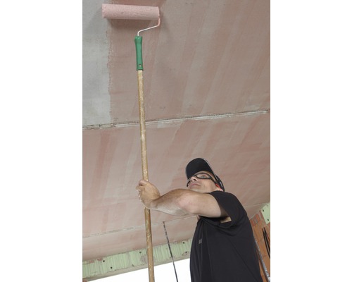 Mann streicht Zimmerdecke mit Farbroller an Stange