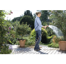 Frau gießt Pflanzen mit einem Gartenschlauch im Garten.