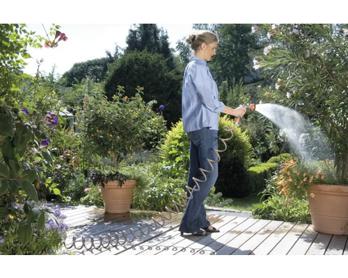 Frau gießt Pflanzen mit einem Gartenschlauch im Garten.