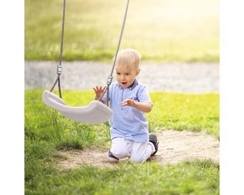 Kleinkind kniet auf einer Wiese und spielt mit einer Schaukel.