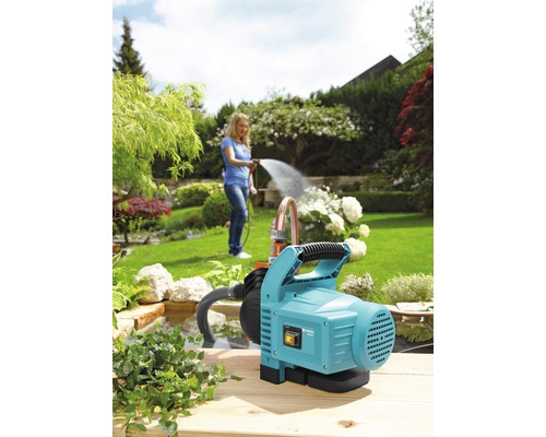 Garten mit Gartenpumpe und Frau beim Bewässern der Pflanzen
