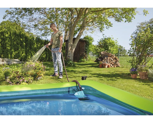 Ein Mann bewässert mit einem Gartenschlauch Blumen neben einem Pool im Garten.