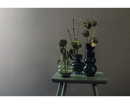 Szene mit grauer Textiltapete und einem Arrangement aus grünen Glasvasen mit Blumen auf einem kleinen Tisch