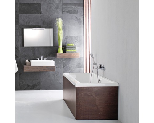 Badezimmer mit Badewanne, Waschtisch, Spiegel und Regalen vor grauer Steinwand