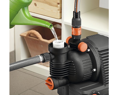 Eine Gartenpumpe wird mit einer Gießkanne mit Wasser befüllt.