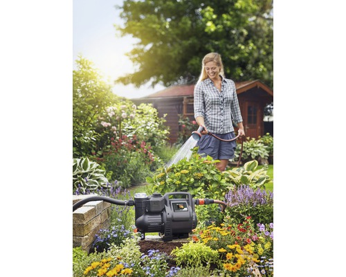 Eine Frau bewässert einen Garten mit einer Gartenpumpe in einem blühenden Garten.