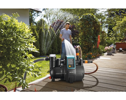 Garten mit Hauswasserwerk und Person, die mit einem Schlauch gießt