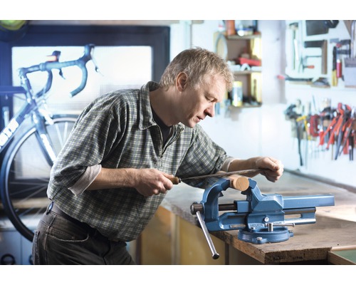 Mann arbeitet mit einer Feile an einem Werkstück, das in einem Schraubstock eingespannt ist.