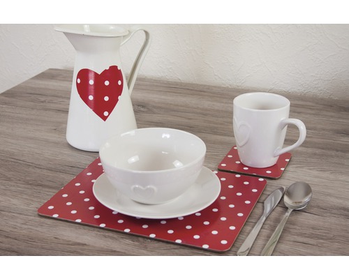 Dekoratives Tischgedeck mit Krug, Schüssel, Tasse, Tellern, Untersetzern und Besteck auf einem Tisch