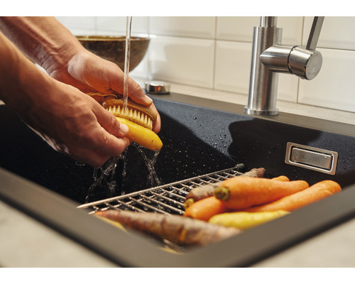 Person wäscht Karotten in einer schwarzen Spüle mit Abtropfgitter unter einem Wasserhahn