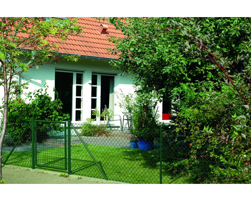Ein grüner Maschendrahtzaun mit Tor umgibt einen Garten vor einem Haus.