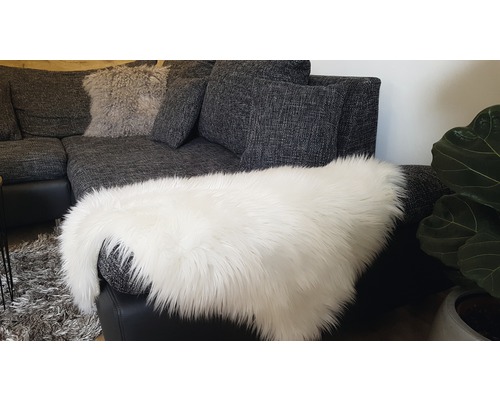 Graues Ecksofa mit Kissen und einem weißen Kunstfellteppich