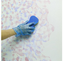 Eine Person mit Handschuhen tupft mit einem Schwamm Farbe auf eine Wand.