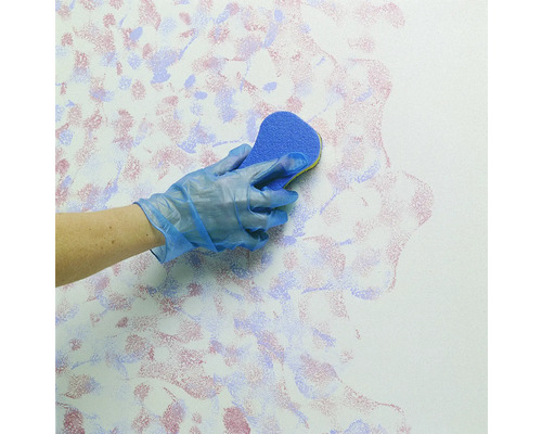 Eine Person mit Handschuhen tupft mit einem Schwamm Farbe auf eine Wand.