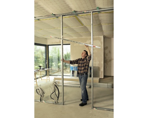 Mann montiert Metallständerwerk mit Messwerkzeug in einem Raum.