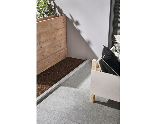 Szene mit Holzpflanzkasten, Sitzgelegenheit und grauen Terrassenplatten.