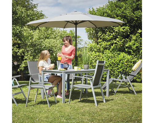 Gartenszene mit Esstisch, Stühlen, Liegestuhl und Sonnenschirm auf einer Rasenfläche