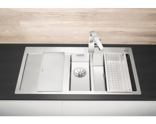 Edelstahlspüle mit Abtropfschale, Schneidebrett und Wasserhahn auf einer Küchentheke.